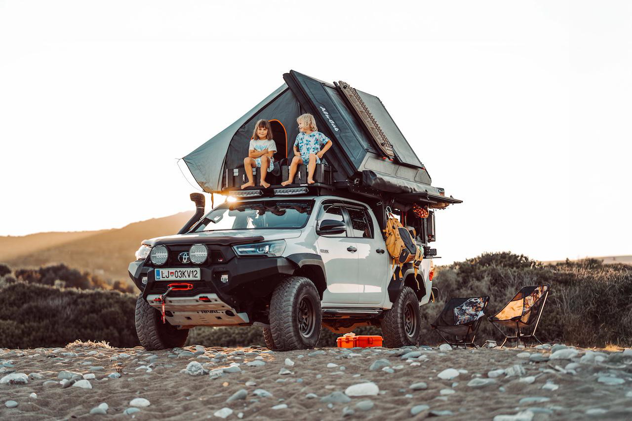Familie beim Campen mit Alu-Cab Aufbau am Strand bei Sonnenuntergang
