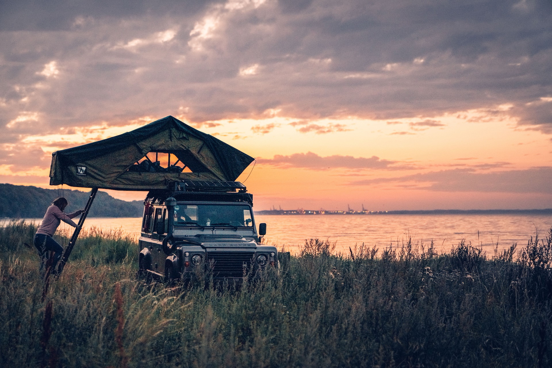 Land Rover Defender mit VICKYWOOD Dachzelt bei Sonnenuntergang am Wasser