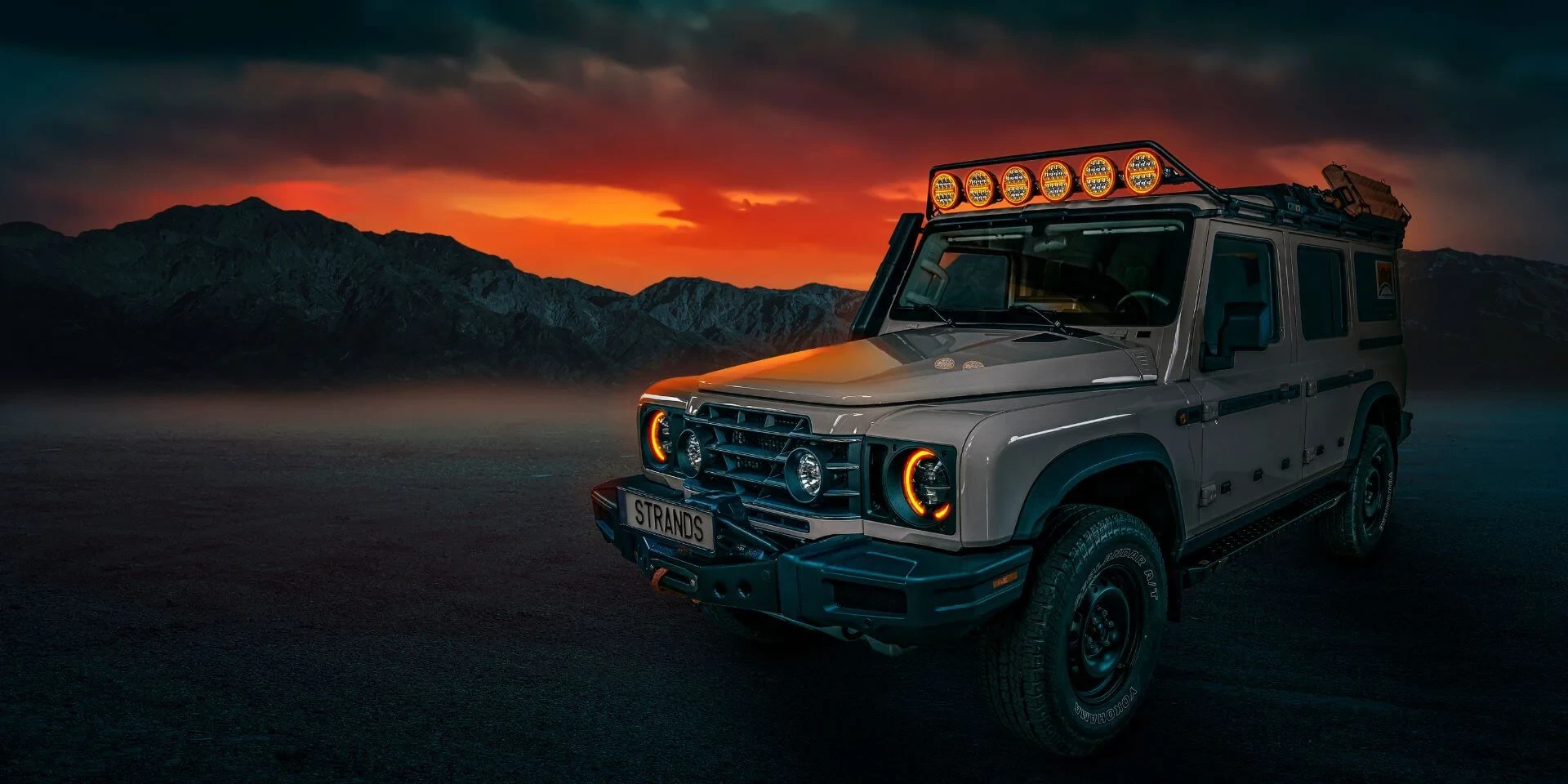 Overland-Fahrzeug mit fünf Strands-Zusatzscheinwerfern auf dem Dachträger bei Sonnenuntergang
